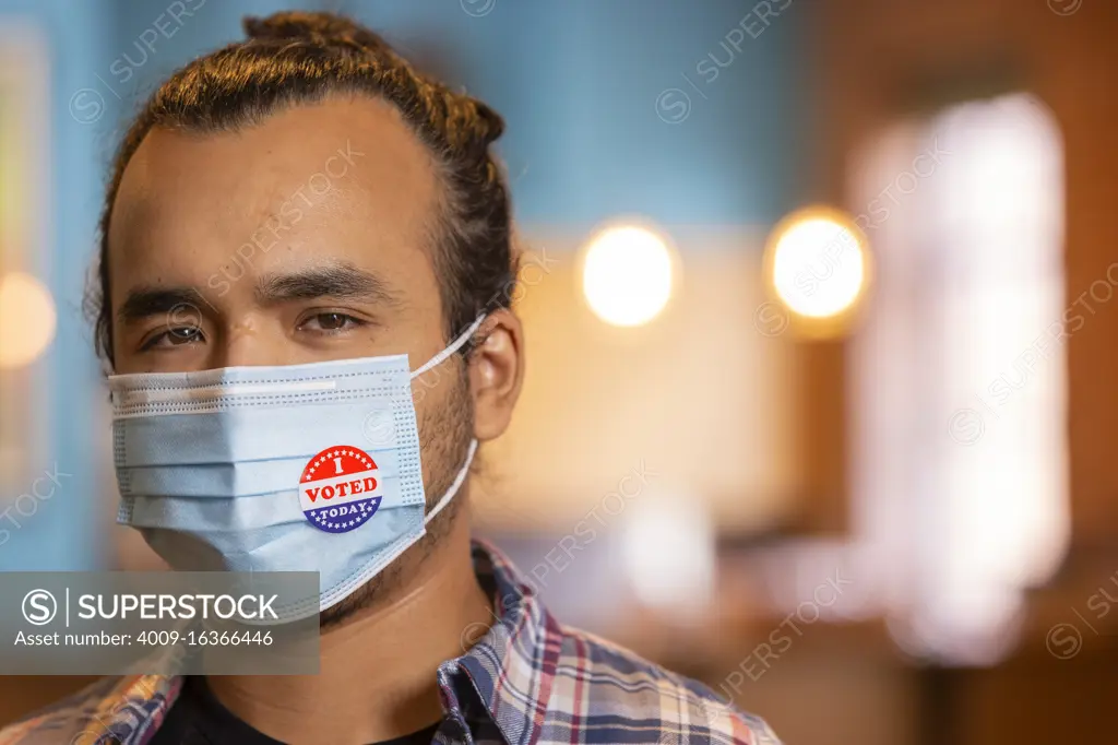 Indoor portrait of a Hispanic male wearing a mask and an I Voted Today sticker on the mask