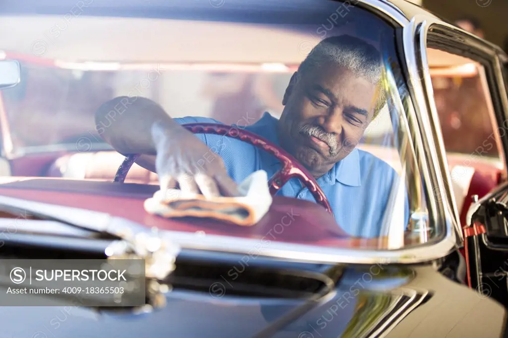 Older man sitting in drivers seat of 1960 Oldsmobile Super 88 Holiday Sport Sedan, wiping down dash with dust cloth 