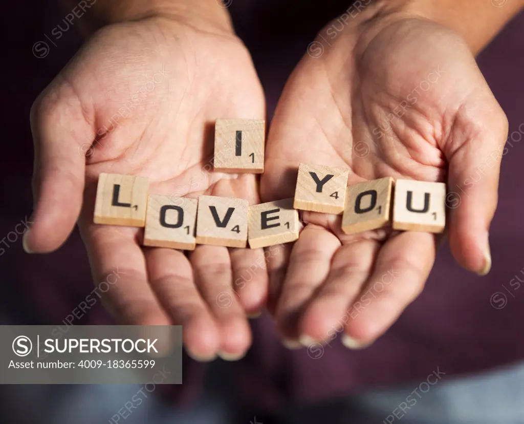 Detail shot of woman holding loose scrabble pieces with the  phrase I Love You” spelled out on the little wooden blocks. Love