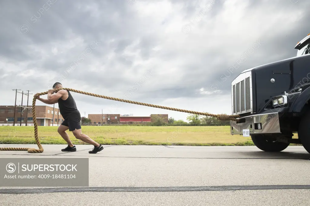 Muscular Hispanic man wearing tank top, Pulling semi truck with large tow rope 