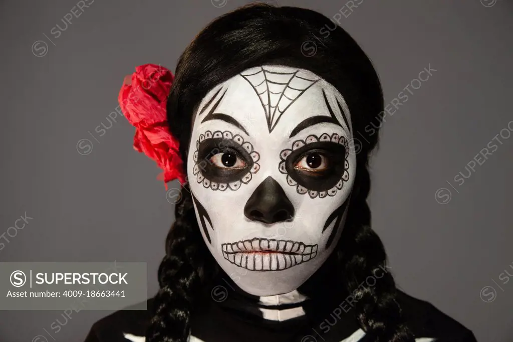 Portrait of a woman dressed up in for Halloween and Day of the Dead Dia de los Muertos with skull face paint. Looking into camera.