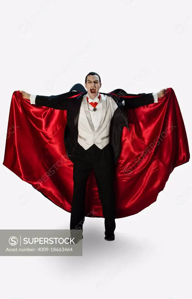 Portrait of a vampire against a white background holding his cape out hissing, looking into camera