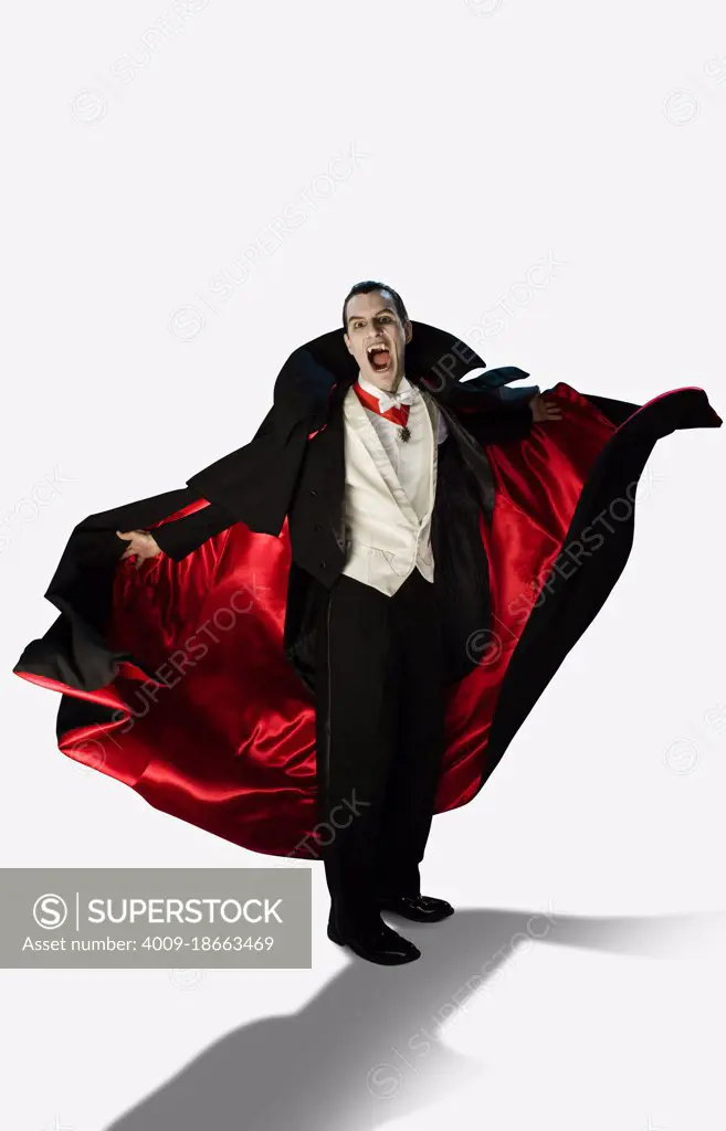 A vampire against a white background holding his arms out at camera with mouth wide open