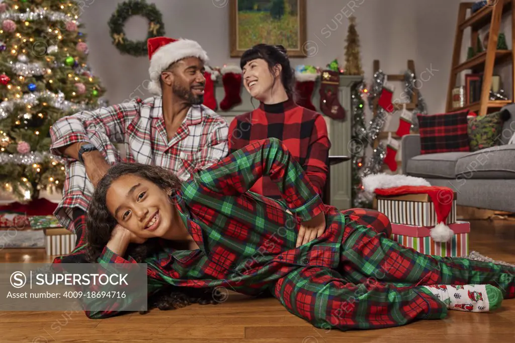 Portrait of a young African American girl laying on the floor looking into camera with her parents in the background.Christmas themed.