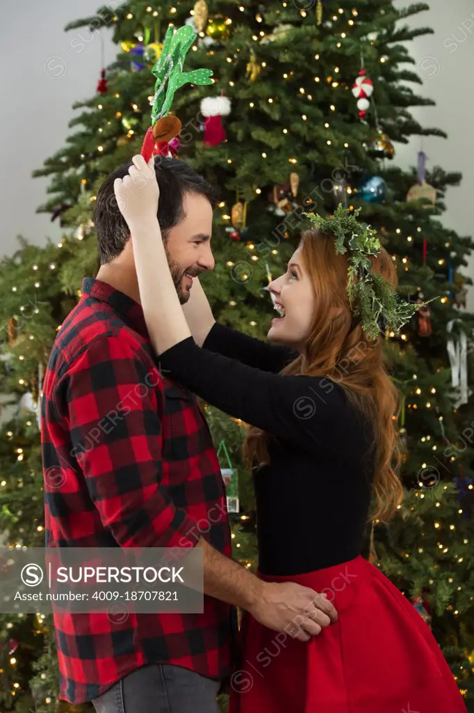 Happy Caucasian couple flirting in front of Christmas tree.