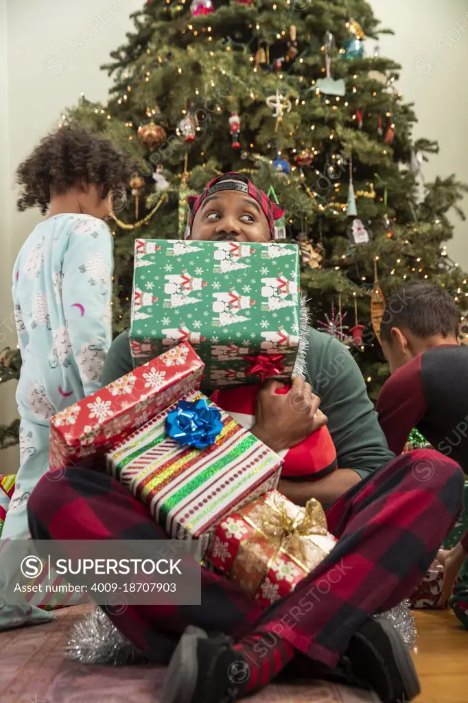 Man playing with his family in front of Christmas tree.