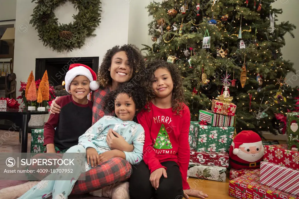 Mother sitting with her three children smiling at camera in front of Christmas tree. 