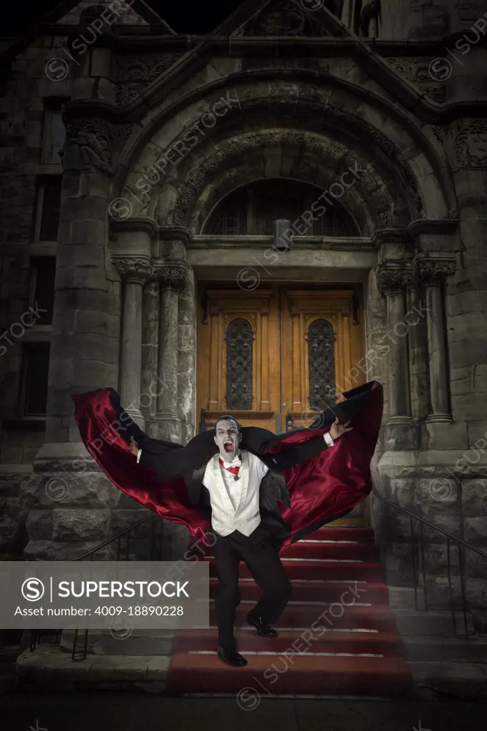 Count Dracula showing fangs and holding his cape out while running towards camera down stairs of stone building 