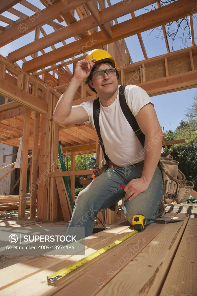 Man using a tape measurer to measure a piece of wood at a residential construction site