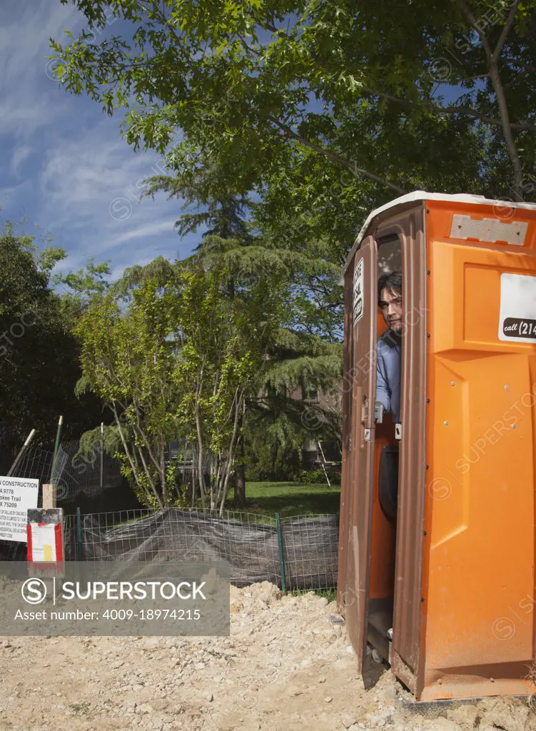 Man looking out the door of a portable toilet at a residential construction site