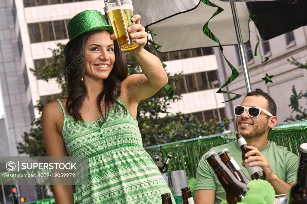 Young woman raising her beer glass while at party on balcony for St Patrick's Day