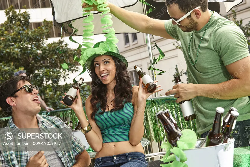 Young women with beer celebrating St. Patrick's Day with friends on balcony during the day.