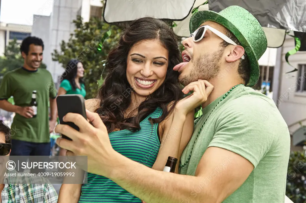 Fun couple taking a selfie while partying with friends all wearing green clothing for St Patrick's Day