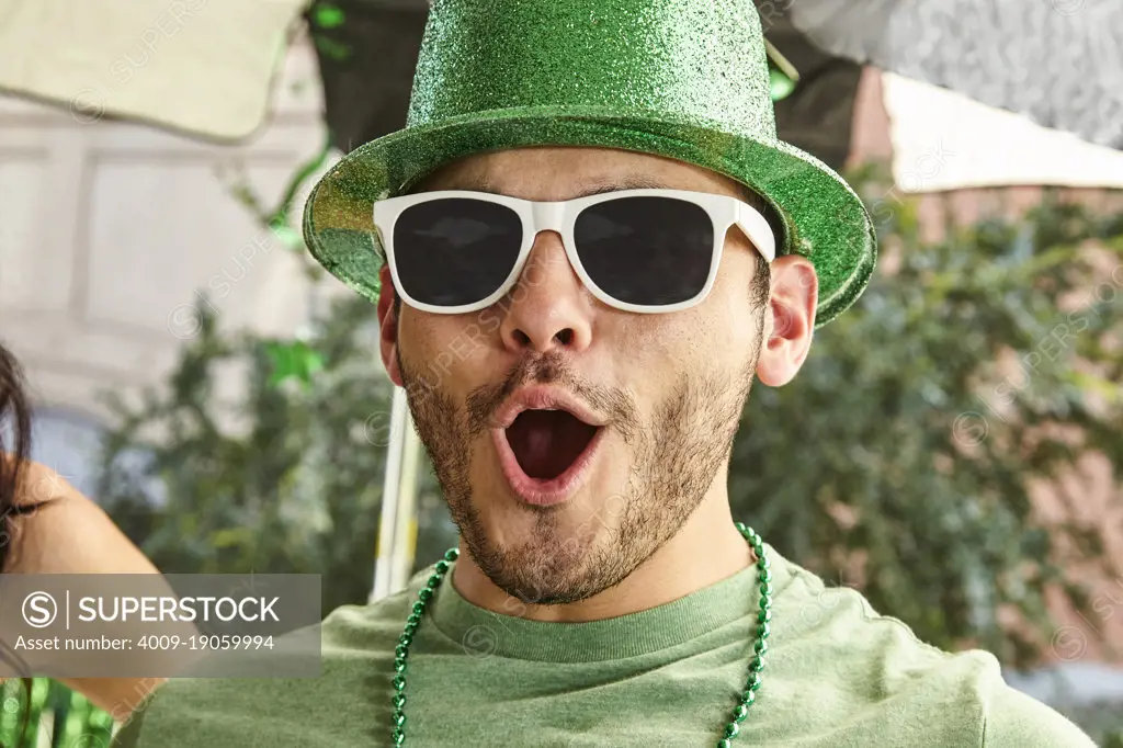 Happy St. Patrick's Day man in a green hat and sunglasses screaming in celebration while at party