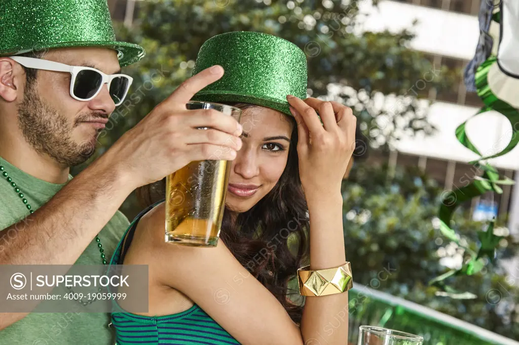Man and woman wearing green sparkle hats dancing while holding beer bottles for St. Patrick's Day Party
