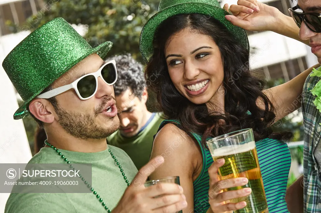 Group of people holding beer glasses dancing and wearing green themed St. Patrick's Day clothing. 