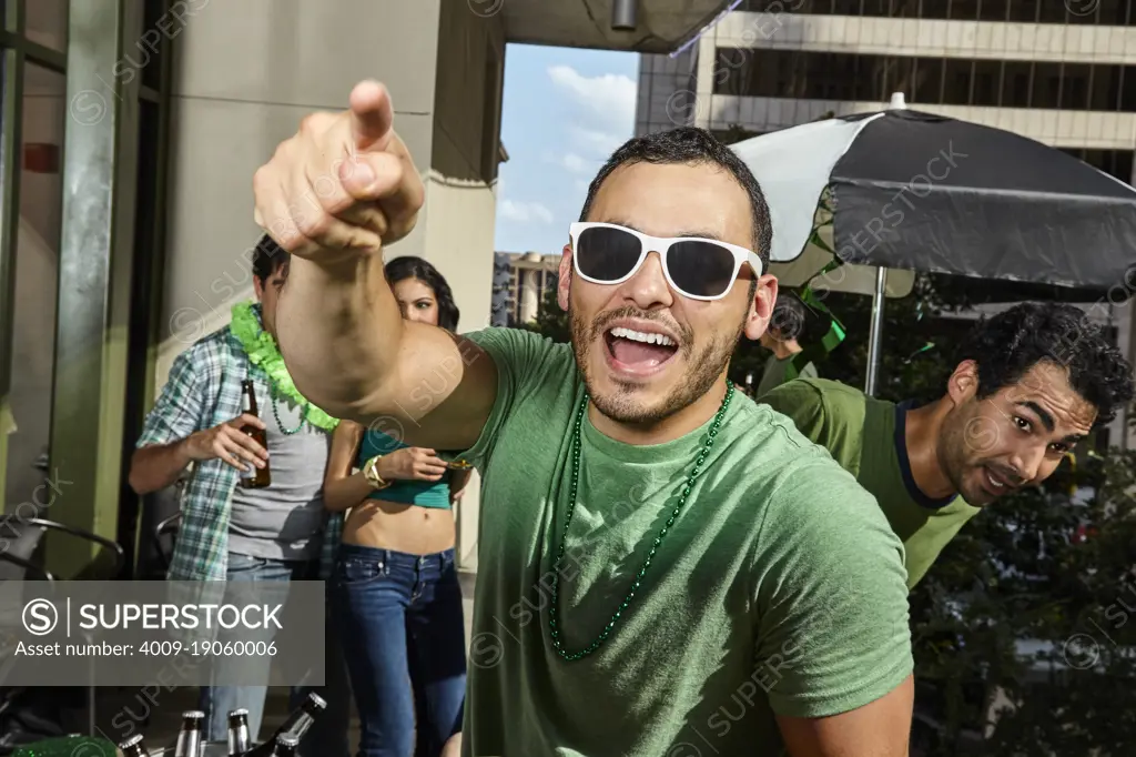 Man smiling and pointing at cameras while at St Patrick's day party. 