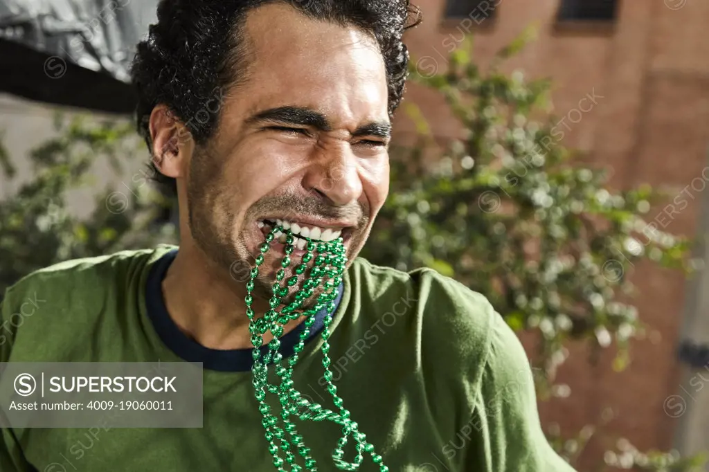 Happy man with green St Patrick's Day beads in his mouth dancing at a party.