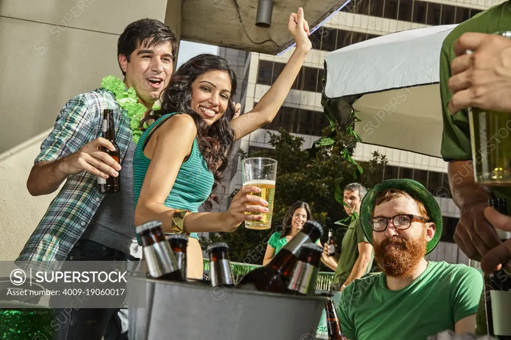 Friends dancing and drinking beer on outdoor patio while watching St Patrick's Day parade.