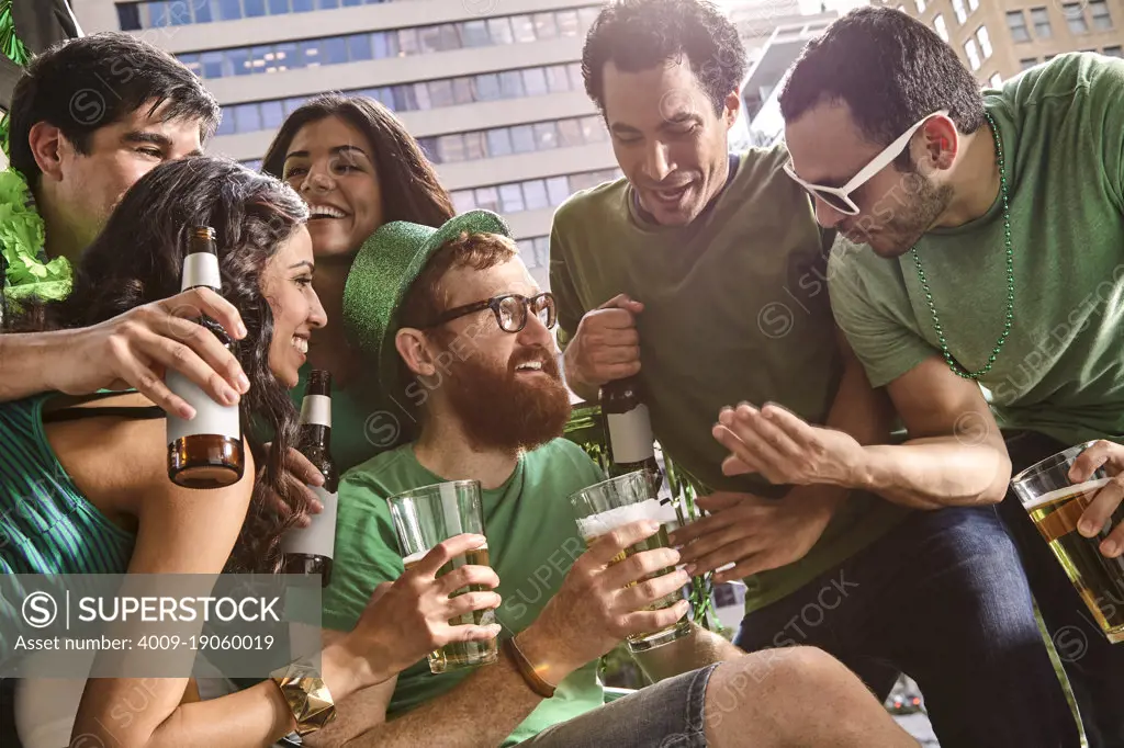 Group of friends hanging out on balcony of bar enjoying the St Patrick's Day festivities drinking beer.