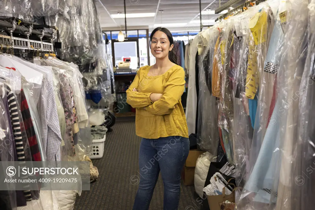 Portrait of laundromat owner in her shop looking into camera with pride, arms crossed