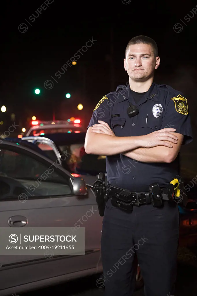 Portrait of Police officer on scene of automobile accident standing in front of wreck with arms crossed 