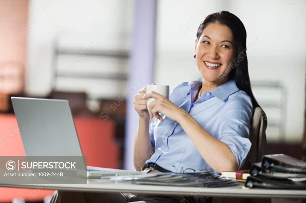 Businesswoman sitting at desk holding a cup of coffee