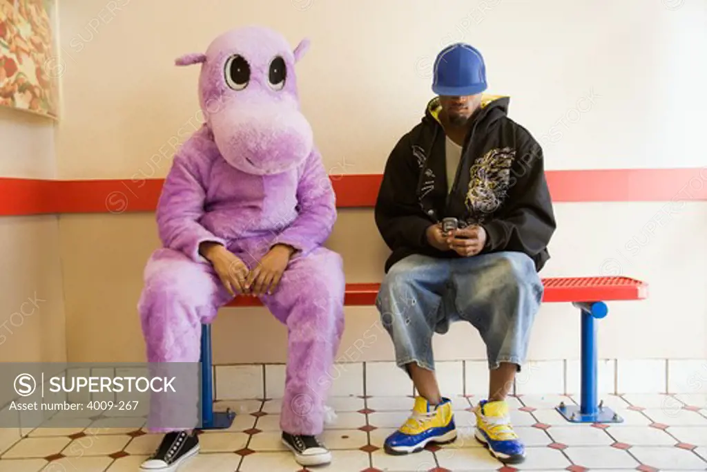 Person in hippo costume sitting next to a man text messaging on a mobile phone