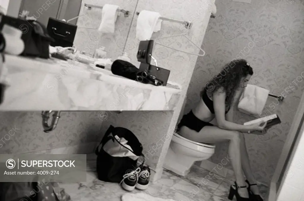 Young woman reading a magazine on a toilet seat