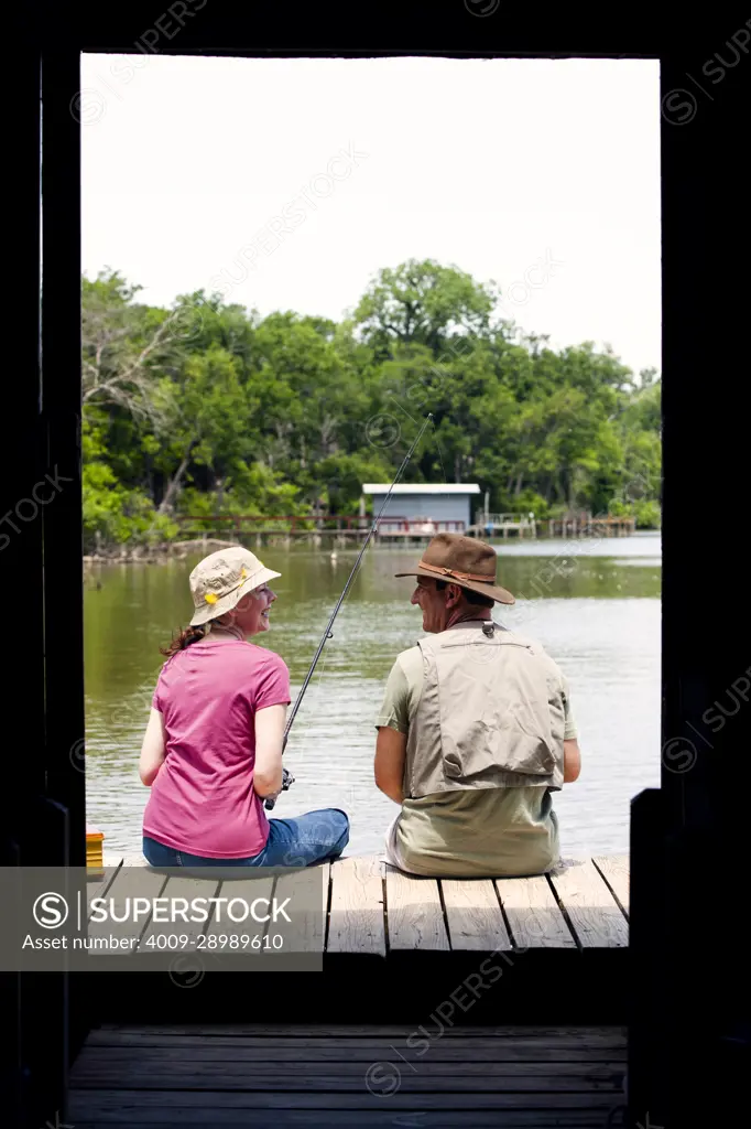 Older couple with fishing poles and accessories sitting on edge of