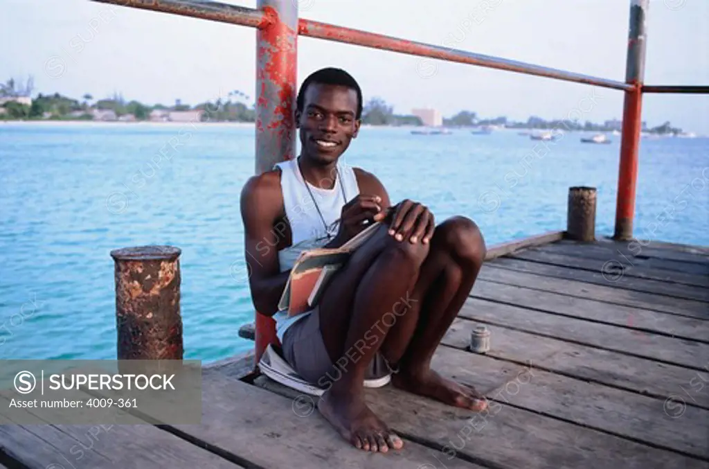 Young man sitting on a dock and writing in journal, Barbados