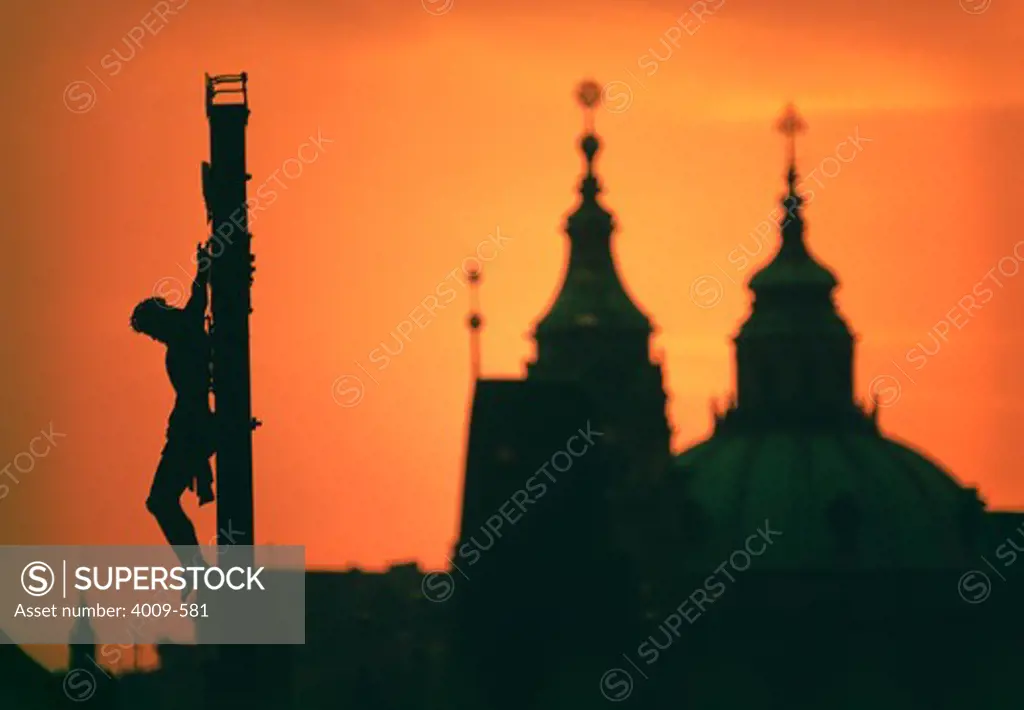 Silhouette of statue of Jesus Christ and a cathedral at sunset, Charles Bridge, Prague, Czech Republic