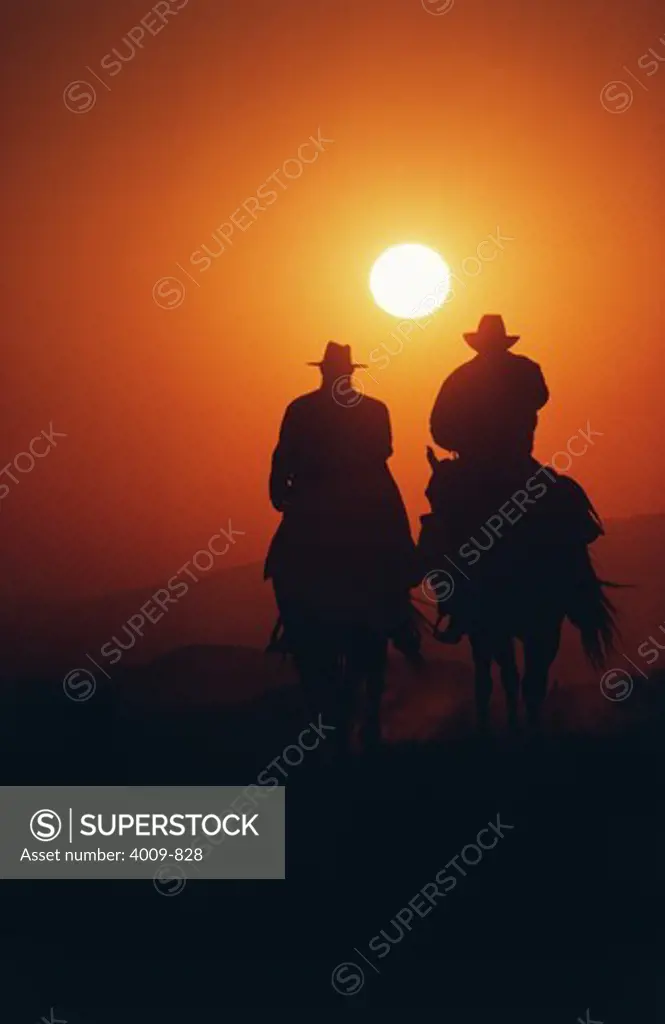 Silhouette of two cowboys riding their horses at sunset, Texas, USA