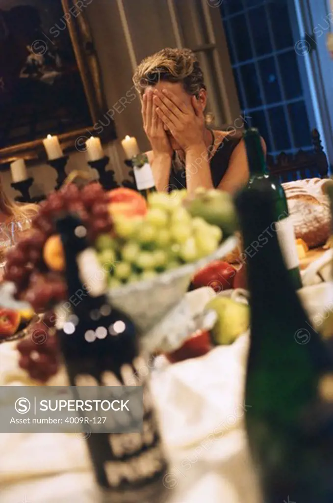 Woman covering her face at a dining table in a dinner party