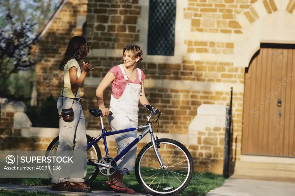 Young woman walking with a bicycle and talking to her friend in the university campus