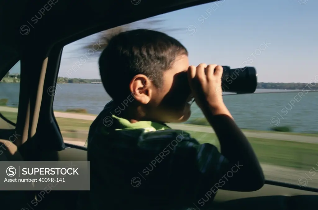 Boy sitting in a car and looking through binoculars