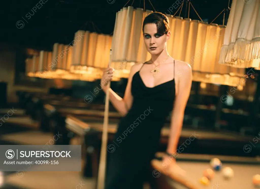 Young woman in evening gown holding a pool cue and leaning against a pool table