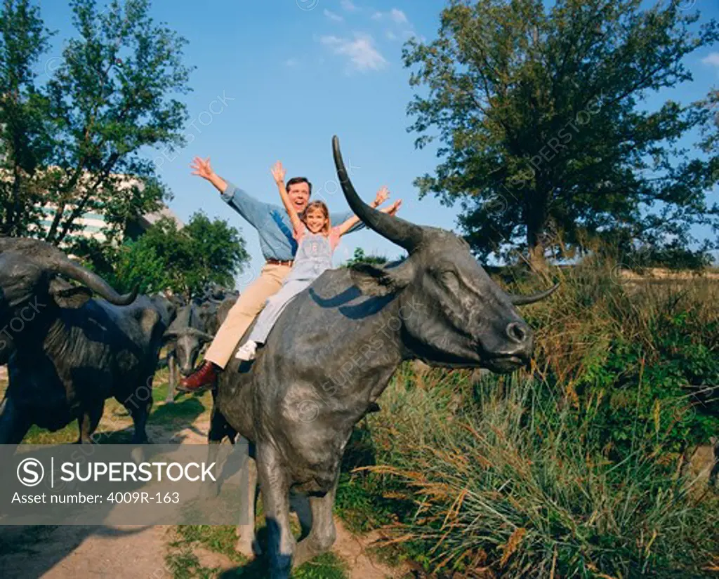 Man with his daughter sitting on a cow's sculpture