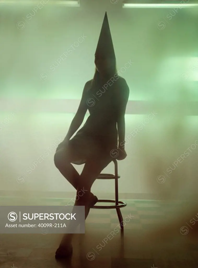 Silhouette of a woman wearing a dunce cap and sitting on a bar stool