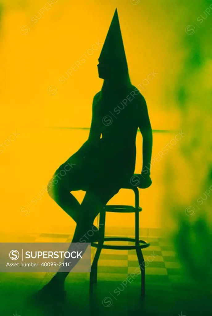 Silhouette of a woman wearing a dunce cap and sitting on a bar stool