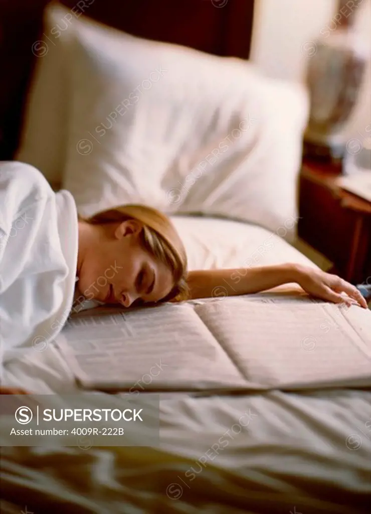 Young woman sleeping on the bed near a newspaper