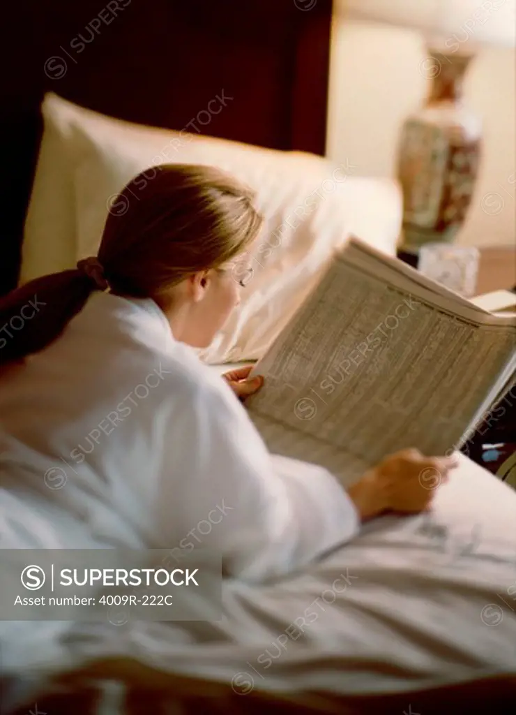 Young woman reading a newspaper on the bed