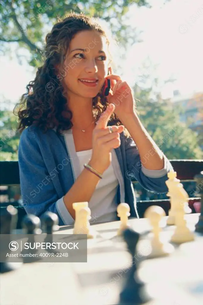 Young woman talking on the phone while playing chess