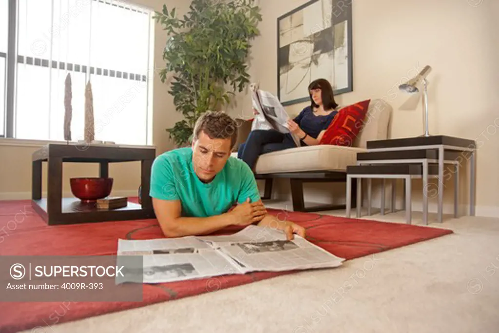 Couple relaxing at home, reading newspaper