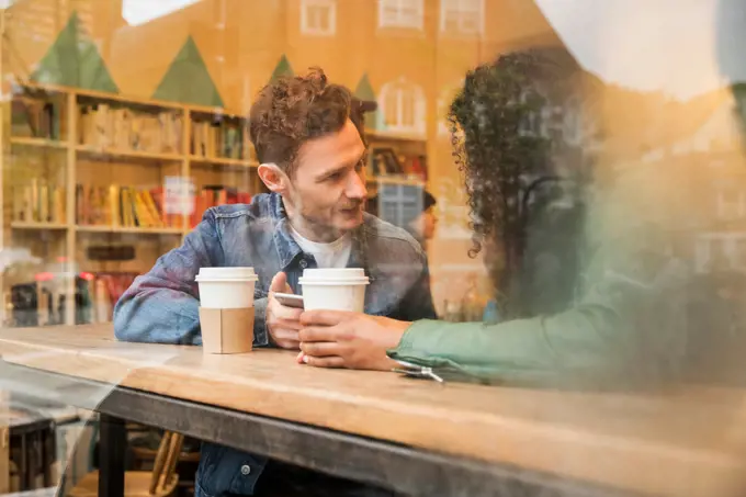 Friends sitting in window of cafe with mobile phone