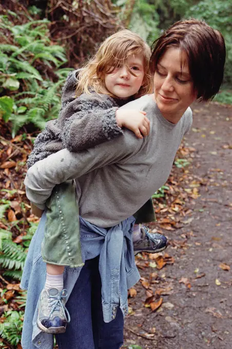 Mother giving young daughter piggyback ride in woods