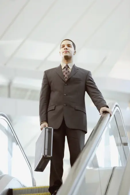 Hispanic businessman carrying briefcase on escalator