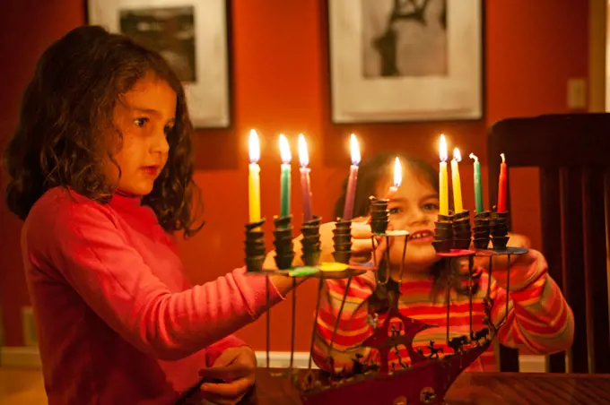 Two young girls lighting Chanukah candles.
