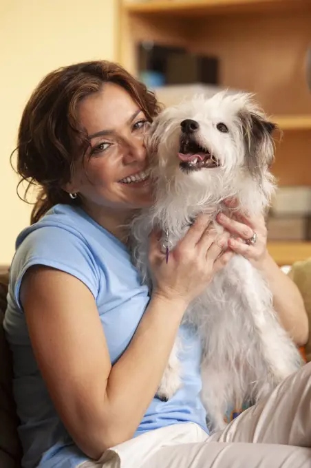 portrait of woman at home sitting on couch holding her pet dog on her lap,  dog looking slightly off camera with mouth open