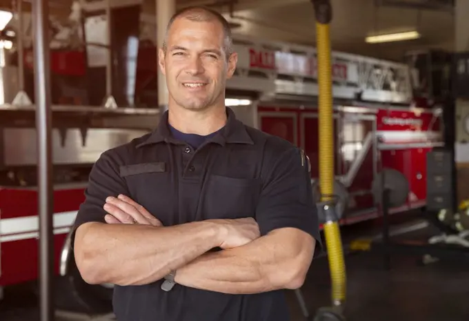 Portrait of Fireman standing in front of firetruck with arms crossed smiling 